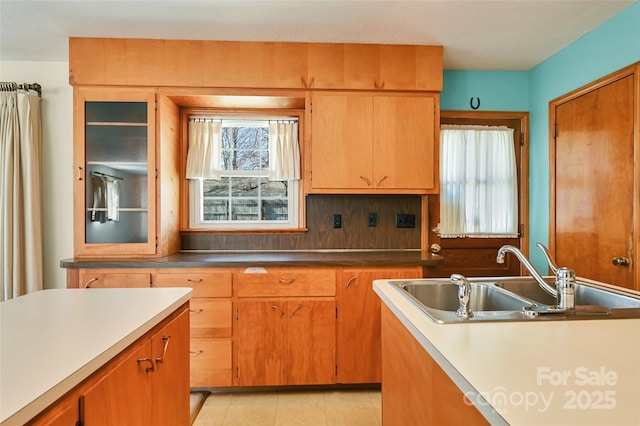 kitchen with light tile patterned floors, backsplash, a sink, and glass insert cabinets