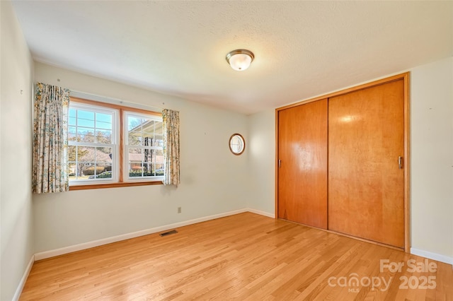 unfurnished bedroom featuring light wood finished floors, baseboards, visible vents, and a closet