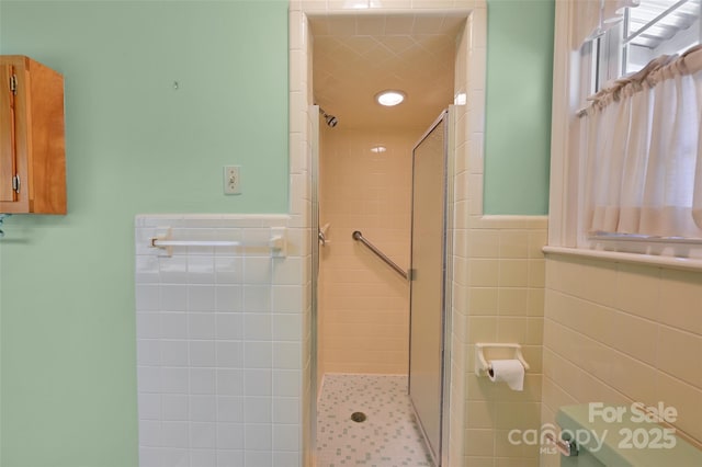 bathroom with a stall shower, a wainscoted wall, and tile walls