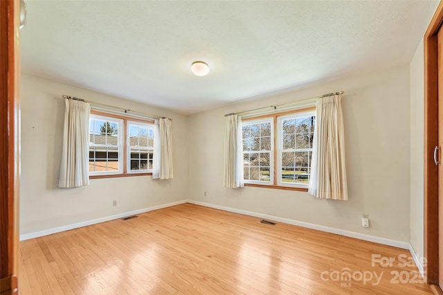 spare room featuring light wood-style floors, visible vents, a textured ceiling, and baseboards