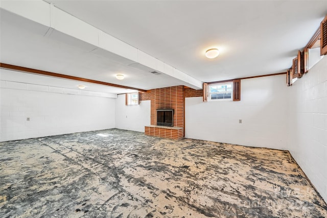 unfurnished living room featuring concrete block wall, a brick fireplace, plenty of natural light, and visible vents