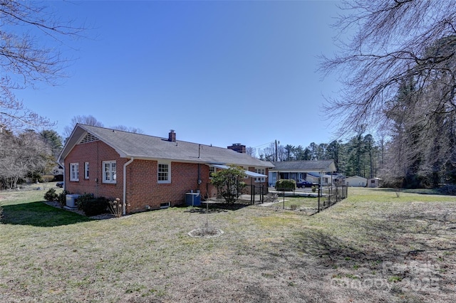 exterior space with central AC unit, brick siding, fence, a yard, and a chimney