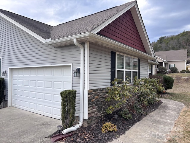 view of side of property with a garage, stone siding, driveway, and a shingled roof