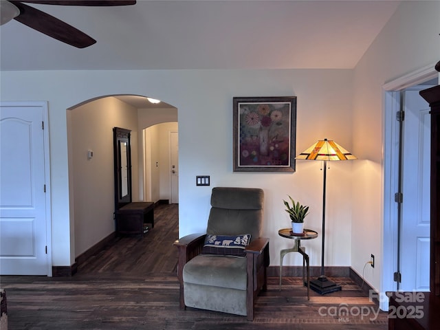 living area with arched walkways, ceiling fan, dark wood finished floors, and baseboards