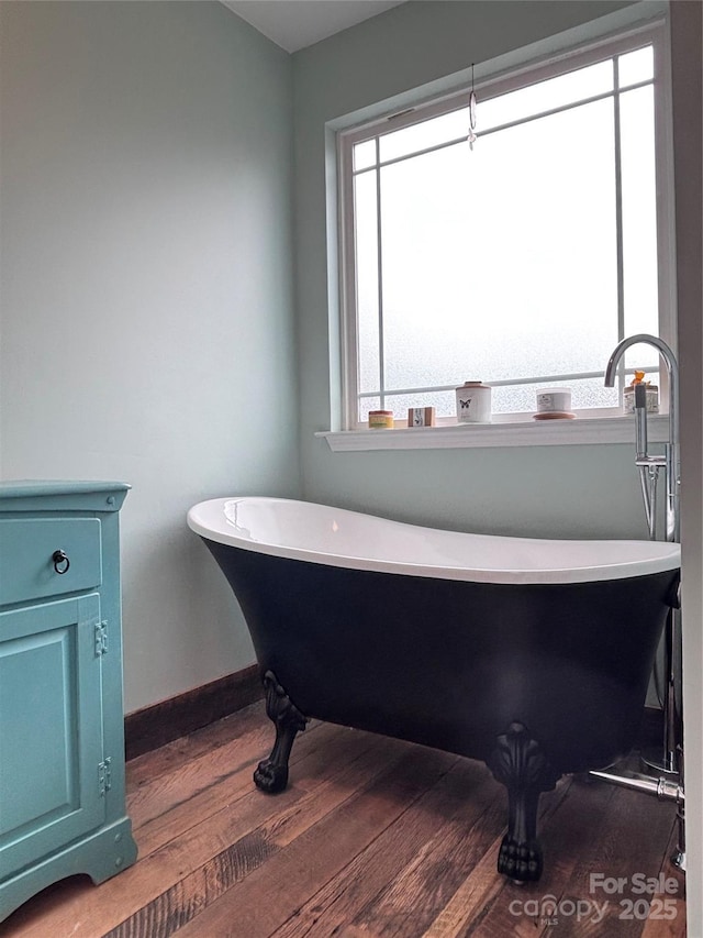 full bathroom featuring baseboards, a freestanding bath, wood finished floors, and a healthy amount of sunlight