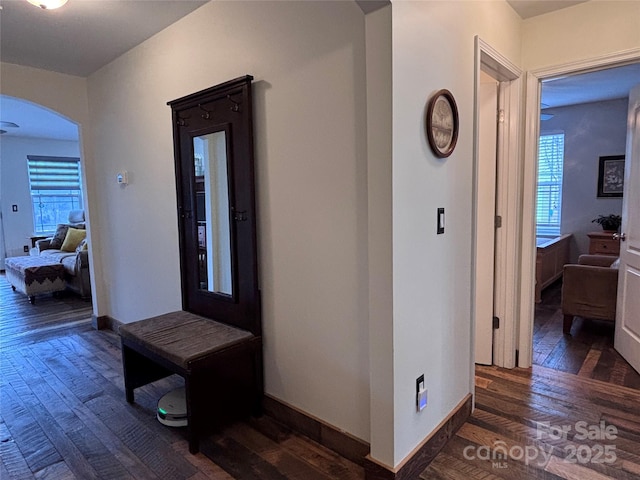 hall with baseboards, arched walkways, and dark wood finished floors