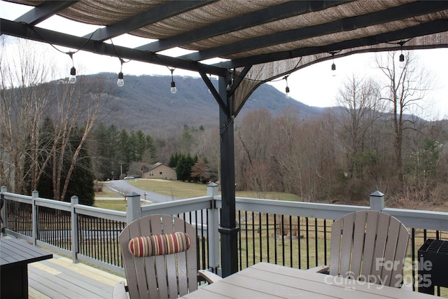 wooden deck featuring a forest view, a mountain view, a pergola, and a yard