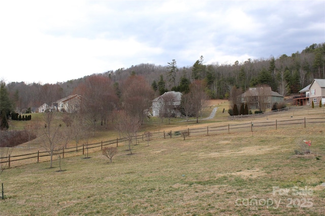 view of yard featuring a rural view, fence, and a wooded view