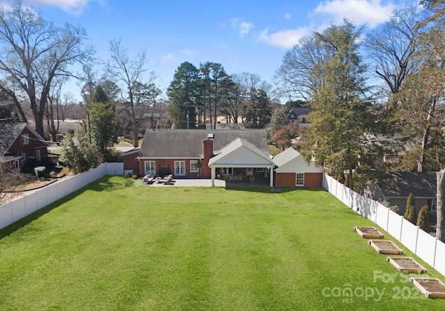 rear view of house with a yard, a vegetable garden, a chimney, a patio, and a fenced backyard