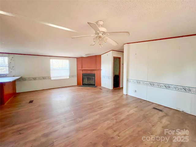 unfurnished living room with a glass covered fireplace, a healthy amount of sunlight, visible vents, and wood finished floors