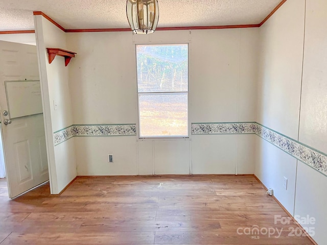 empty room featuring light wood-style floors, crown molding, and a textured ceiling