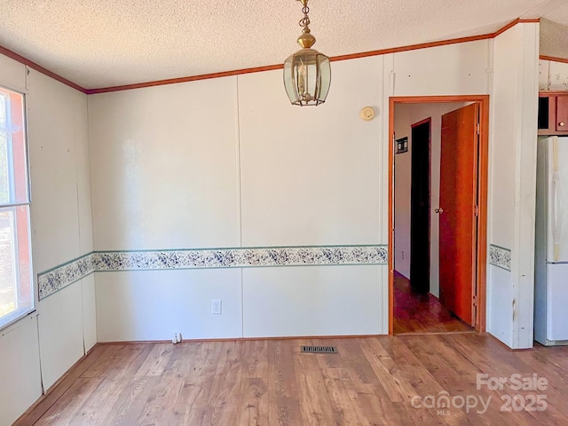 spare room with ornamental molding, a textured ceiling, and light wood finished floors