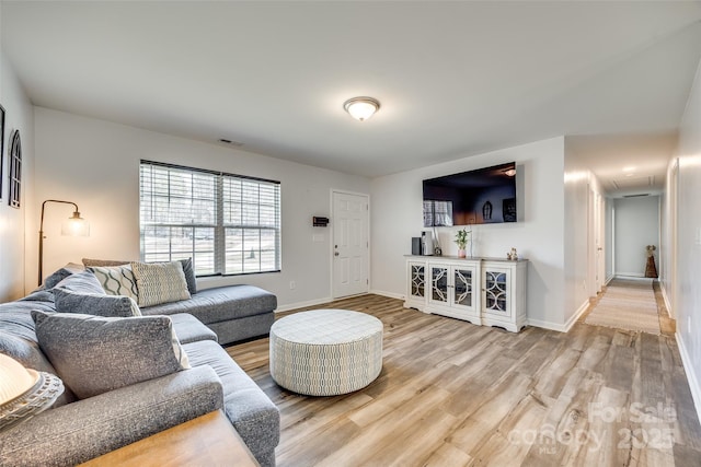 living area with attic access, light wood-type flooring, visible vents, and baseboards