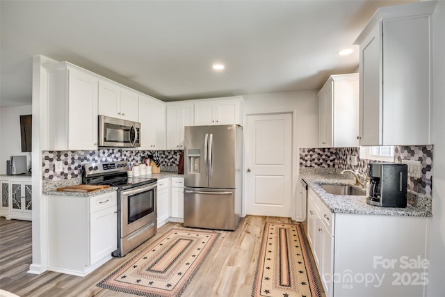 kitchen with a sink, white cabinetry, light wood-style floors, appliances with stainless steel finishes, and tasteful backsplash