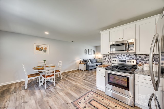 kitchen featuring stainless steel appliances, backsplash, light wood-style floors, white cabinets, and baseboards