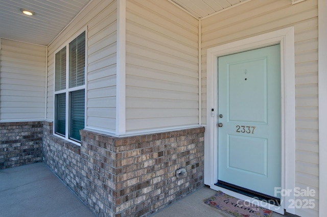 entrance to property featuring a porch and brick siding