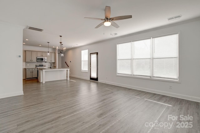 unfurnished living room featuring visible vents, crown molding, baseboards, and wood finished floors