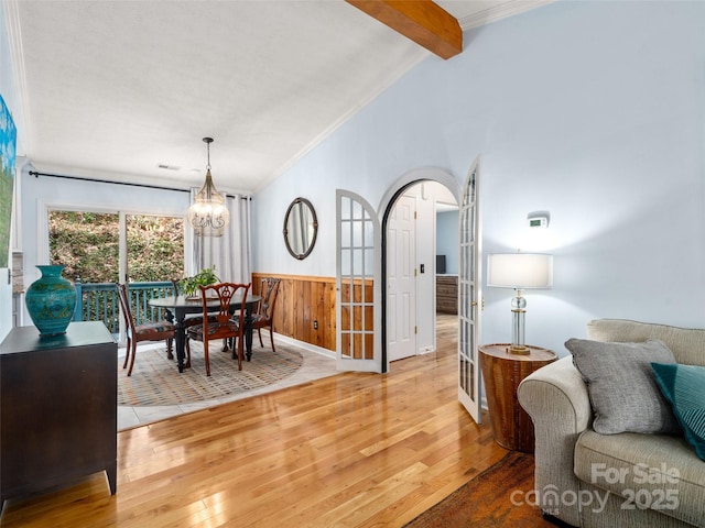 dining space featuring arched walkways, crown molding, vaulted ceiling with beams, wainscoting, and wood finished floors