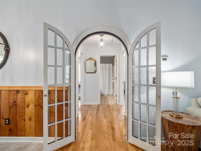 corridor featuring arched walkways and light wood-style flooring