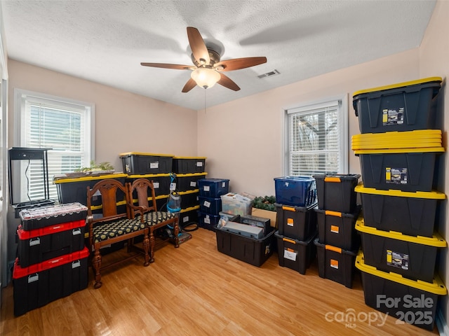 home office with a ceiling fan, a textured ceiling, visible vents, and wood finished floors