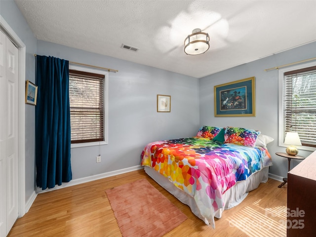 bedroom with a textured ceiling, wood finished floors, visible vents, and baseboards