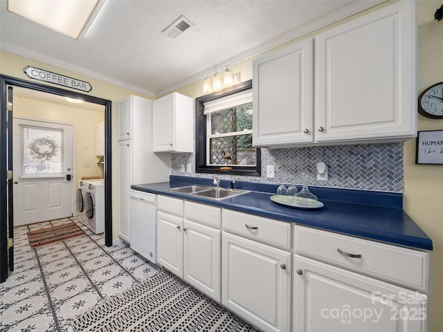 kitchen featuring visible vents, dark countertops, independent washer and dryer, white dishwasher, and a sink