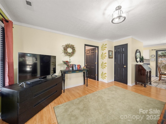 living area with a textured ceiling, ornamental molding, wood finished floors, and visible vents