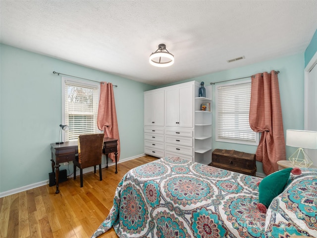 bedroom featuring visible vents, light wood-style flooring, baseboards, and a textured ceiling