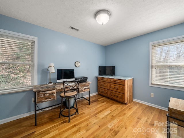 office featuring a textured ceiling, light wood-type flooring, visible vents, and baseboards