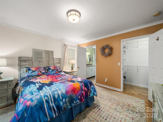 bedroom featuring light wood finished floors, a spacious closet, ornamental molding, a textured ceiling, and baseboards