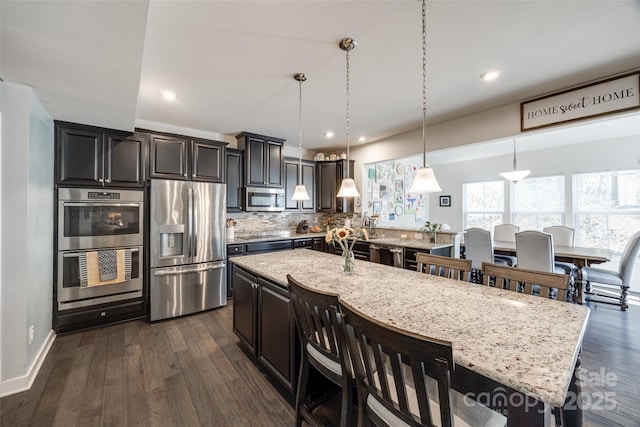 kitchen with appliances with stainless steel finishes, dark wood-style flooring, light stone counters, and tasteful backsplash