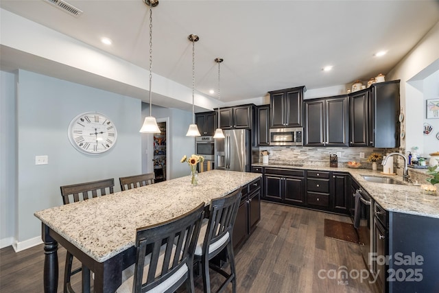 kitchen featuring light stone counters, tasteful backsplash, visible vents, appliances with stainless steel finishes, and a sink