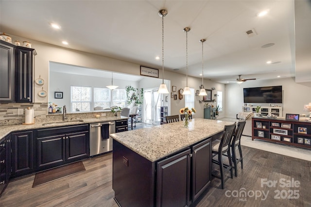 kitchen featuring a kitchen bar, a sink, light stone counters, and stainless steel dishwasher