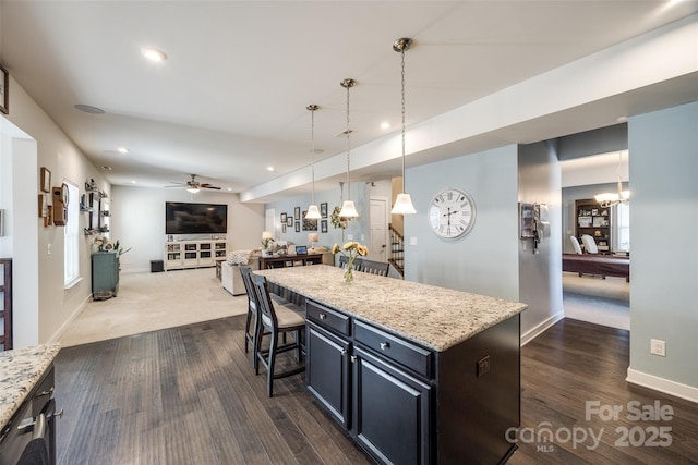 kitchen featuring a breakfast bar, a center island, open floor plan, light stone countertops, and ceiling fan with notable chandelier