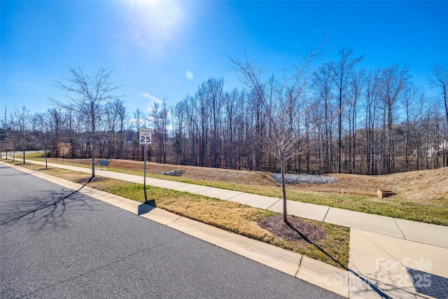 view of road with a wooded view, traffic signs, and sidewalks