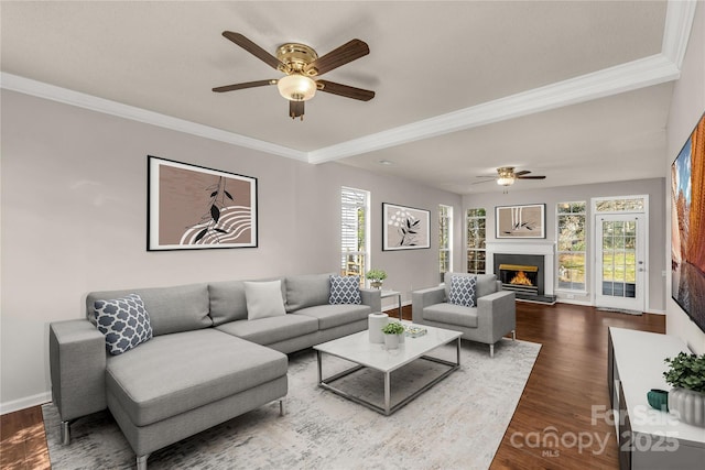 living room featuring ornamental molding, dark wood finished floors, a lit fireplace, and baseboards