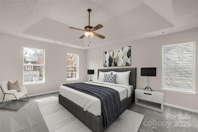 carpeted bedroom with a textured ceiling, a tray ceiling, visible vents, and baseboards