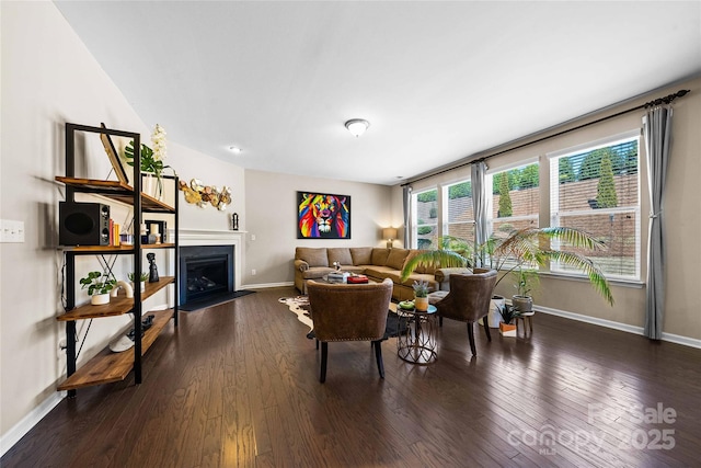 living room featuring a fireplace with flush hearth, baseboards, and dark wood-style flooring