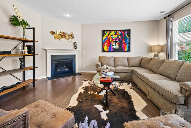 living area featuring a glass covered fireplace, visible vents, baseboards, and wood finished floors