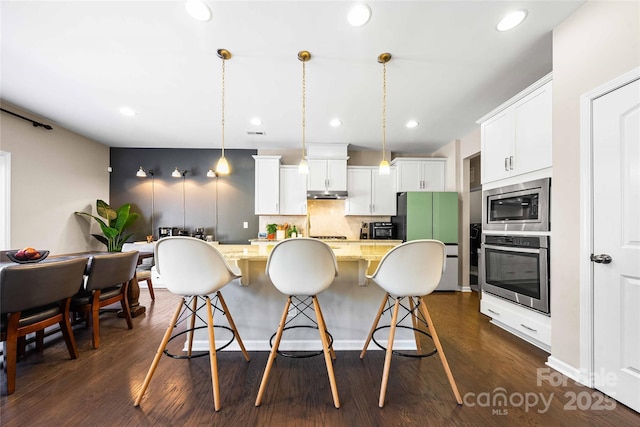 kitchen with backsplash, a center island, under cabinet range hood, a breakfast bar area, and appliances with stainless steel finishes