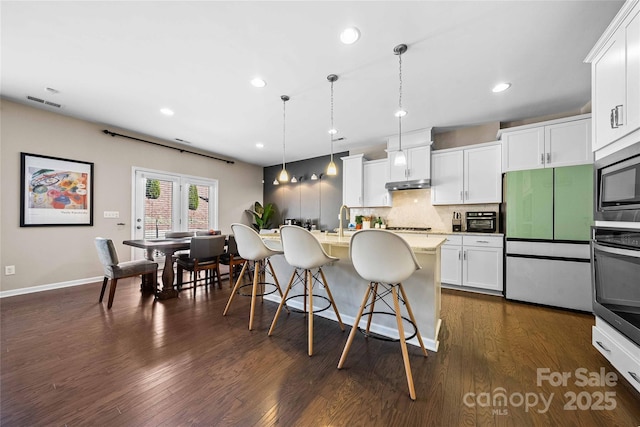 kitchen with a kitchen bar, under cabinet range hood, tasteful backsplash, appliances with stainless steel finishes, and dark wood-style flooring