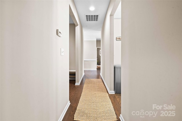 hallway featuring visible vents, dark wood-type flooring, and baseboards