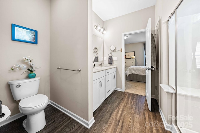 ensuite bathroom with toilet, wood finished floors, a shower stall, baseboards, and vanity