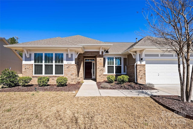 prairie-style home featuring brick siding, a front lawn, a garage, and roof with shingles