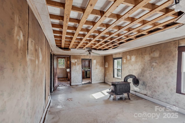 misc room featuring a ceiling fan, a wood stove, and unfinished concrete flooring