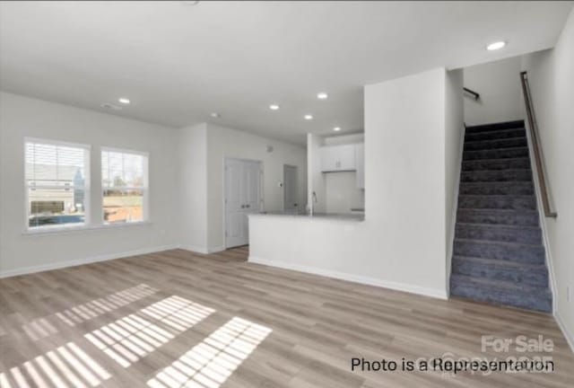 unfurnished living room with recessed lighting, light wood-style flooring, baseboards, and stairs