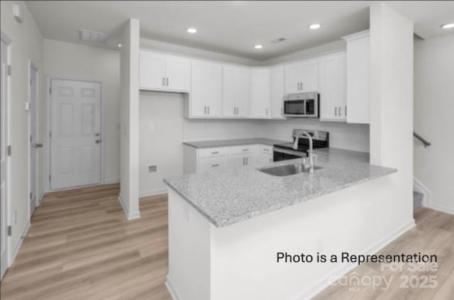 kitchen featuring stainless steel appliances, a peninsula, a sink, white cabinets, and light wood-style floors