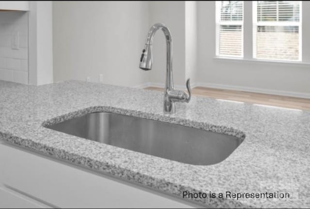 interior details with light stone counters, light wood-type flooring, a sink, and baseboards