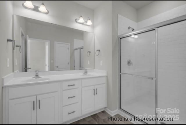 bathroom featuring a stall shower, wood finished floors, a sink, and double vanity