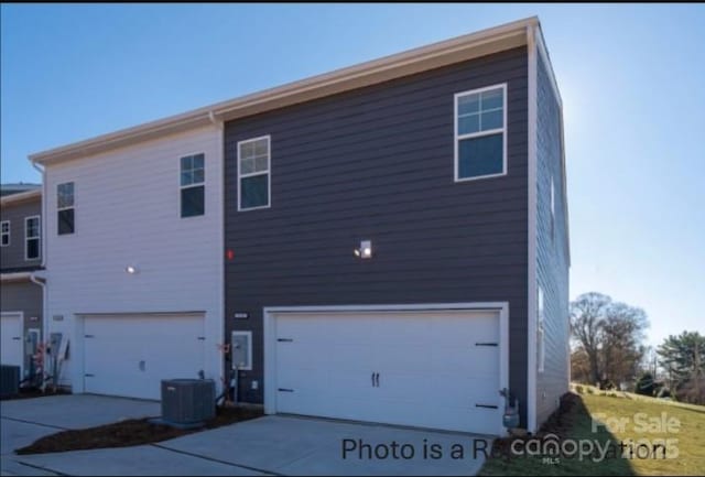 rear view of house featuring driveway, central AC, and an attached garage